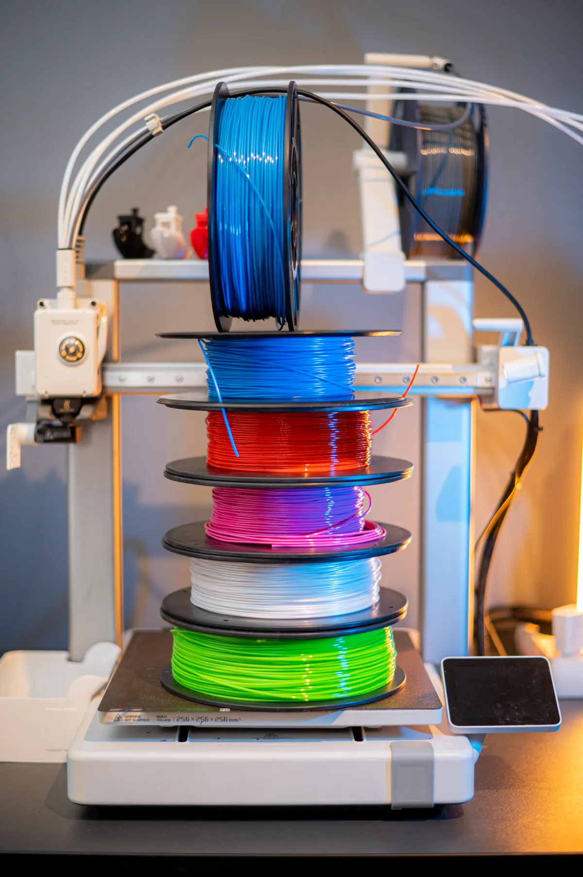 Bobinas de filamento de varios colores apiladas junto a una impresora 3D